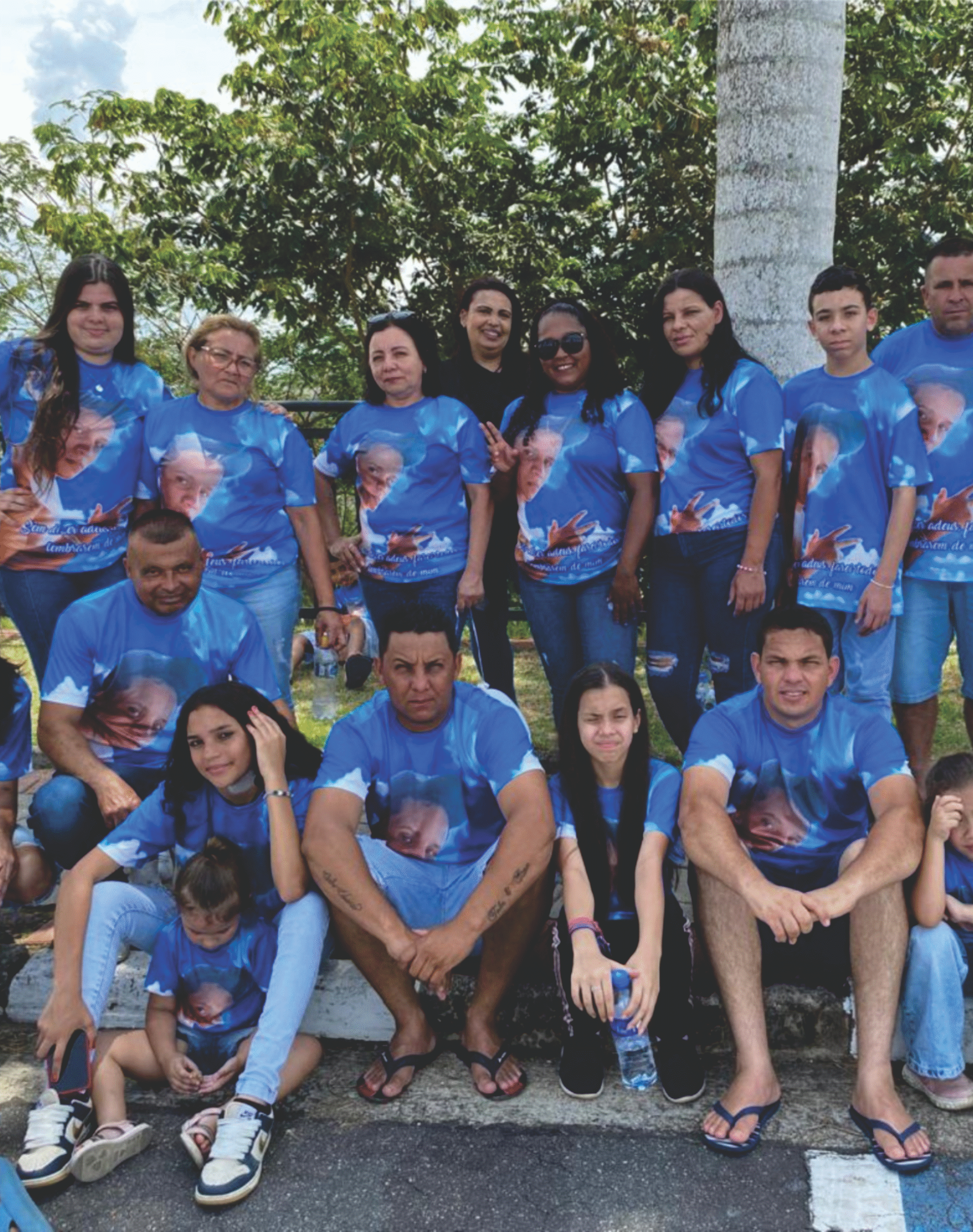 Grande grupo de pessoas reunidas ao ar livre vestindo camisetas personalizadas azuis com estampa fotográfica de homenagem, produzidas pela Maximus Print.