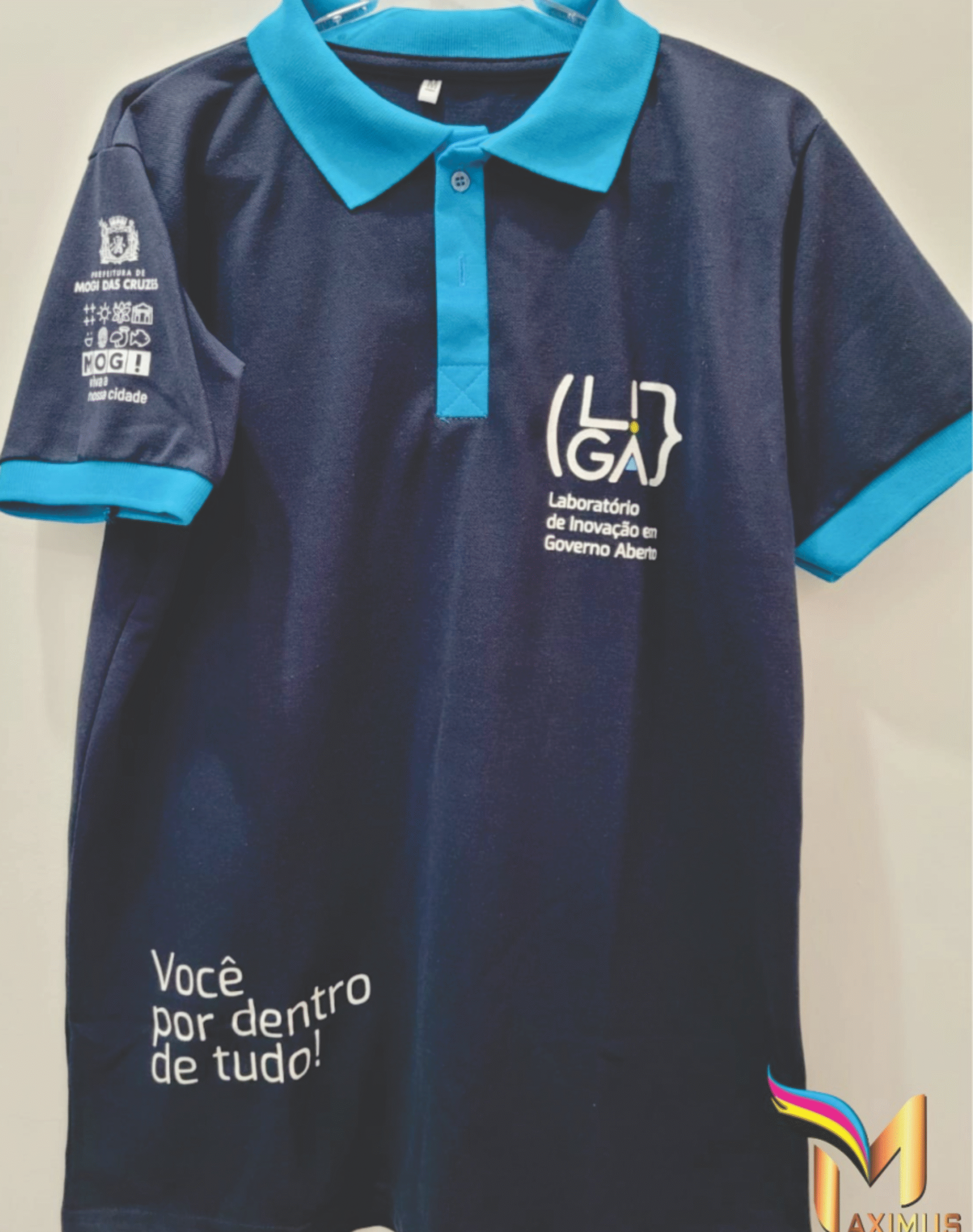 Camiseta polo personalizada azul marinho com gola ciano, exibindo estampas da Prefeitura de Mogi das Cruzes e do Laboratório de Inovação LiGa, produzida pela Maximus Print.