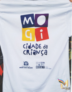 Camiseta branca personalizada com a estampa colorida "Mogi Cidade da Criança" e logotipos da Prefeitura de Mogi das Cruzes, produzida pela Maximus Print.