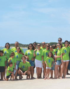 Grande grupo de pessoas na praia vestindo camisetas personalizadas em verde limão com estampas exclusivas, produzidas pela Maximus Print.