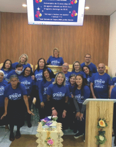Grupo de pessoas em uma igreja vestindo camisetas azuis personalizadas com a frase "Sua graça me basta", produzidas pela Maximus Print para eventos religiosos.