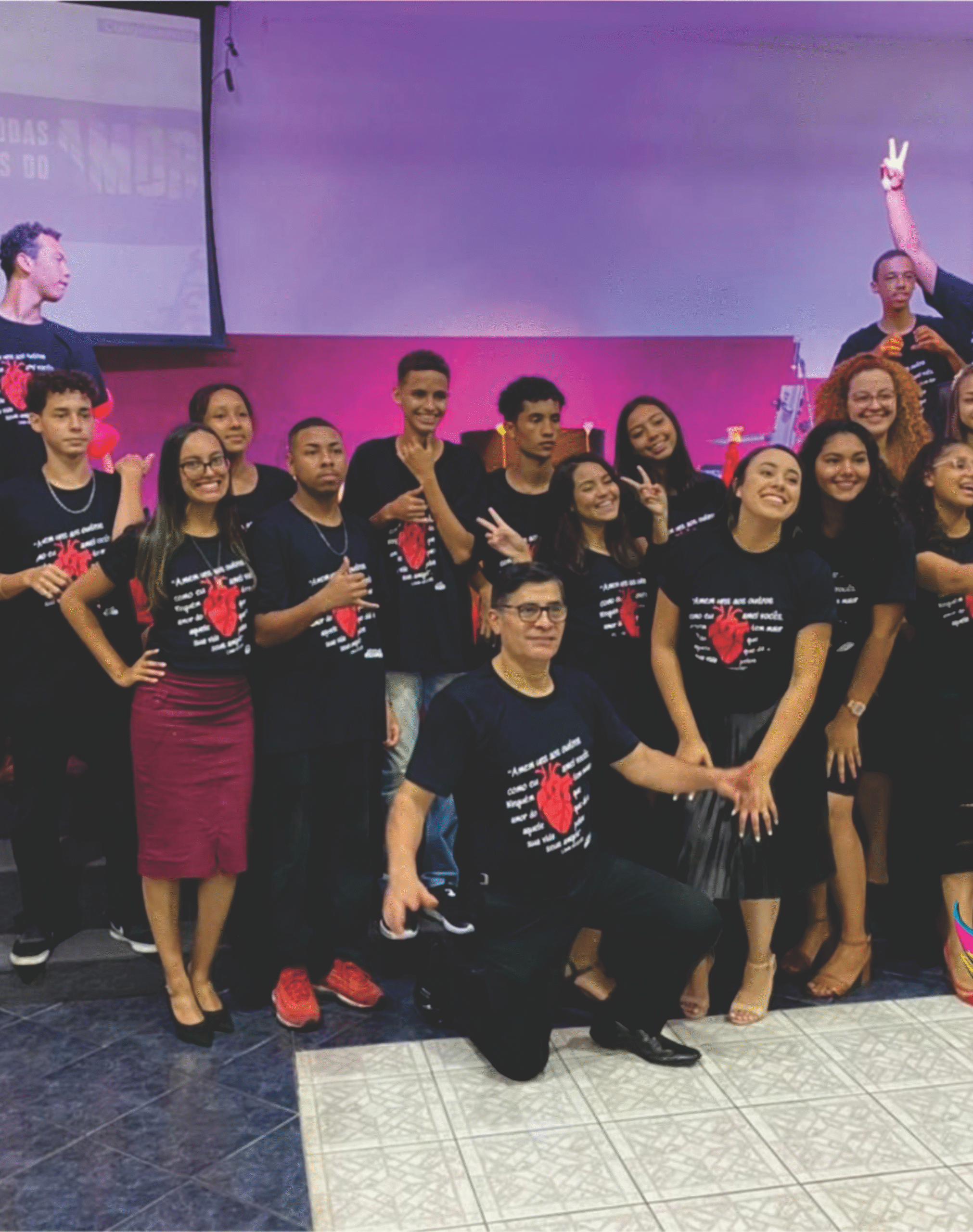 Grupo de pessoas reunidas em um palco vestindo camisetas pretas personalizadas com estampa de um coração vermelho e texto branco, produzidas pela Maximus Print.