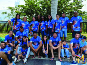 Grande grupo de pessoas reunidas ao ar livre vestindo camisetas personalizadas azuis com estampa fotográfica de homenagem, produzidas pela Maximus Print.