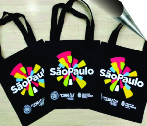 Trio de ecobags pretas personalizadas com estampa colorida da "2ª CONFETUR - Cidade de São Paulo", demonstrando o serviço de brindes personalizados da Maximus Print.